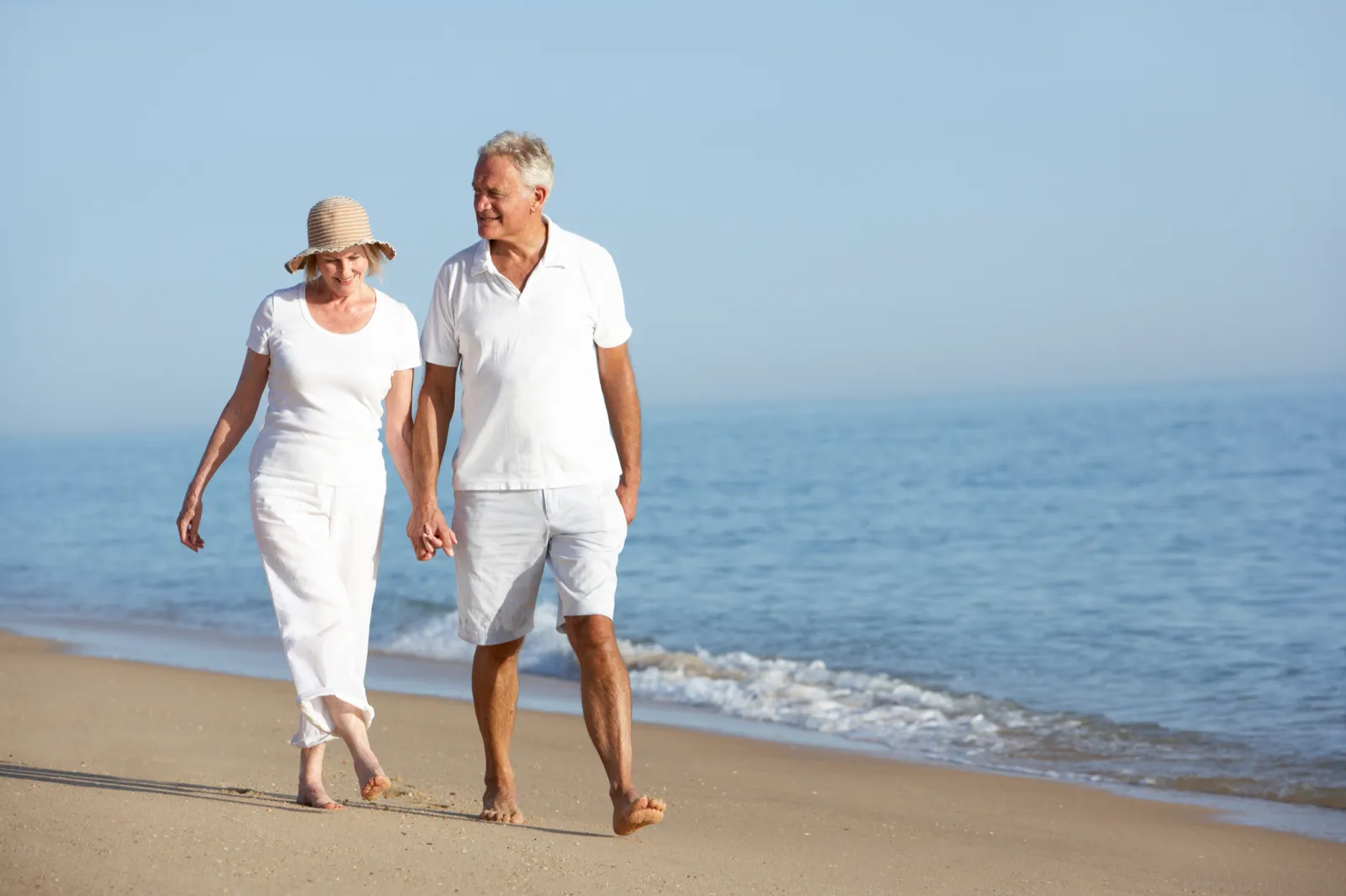 Pareja mayor paseando por la playa, con salud ósea y autonomía